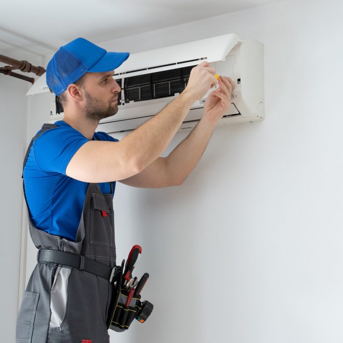 male-technician-overalls-blue-cap-repairs-air-conditioner-wall